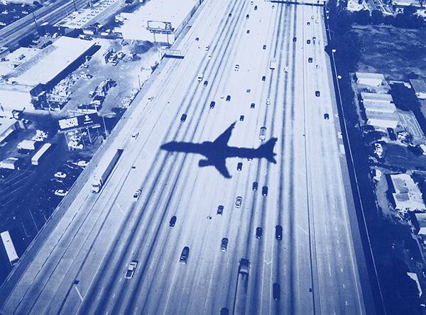 An aerial blue-toned photograph of a highway or runway with an airplane's shadow, from Tim Barber's 'Blues'