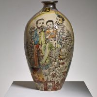 Photograph of a decorative ceramic vase with painted figures, displayed on a white pedestal