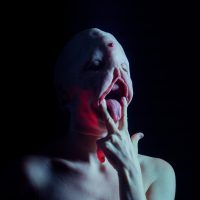 Surreal portrait of a figure with an open mouth and red liquid dripping down, against a dark background