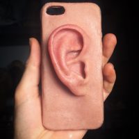 Photograph of a hand holding a smartphone with a case shaped like a human ear