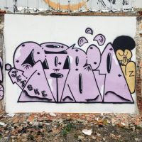 A purple bubble-letter graffiti tag with a cartoon character on a weathered wall, from 'Sabio Stylin' in São Paulo'