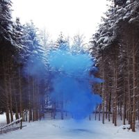 Blue smoke bomb hovering over a snow-covered path lined with pine trees