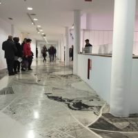 Visitors walking through a gallery with a reflective marble floor and red marking tape on the ground, from Daniel Muñoz's 'Trenches and Other Contraceptives'