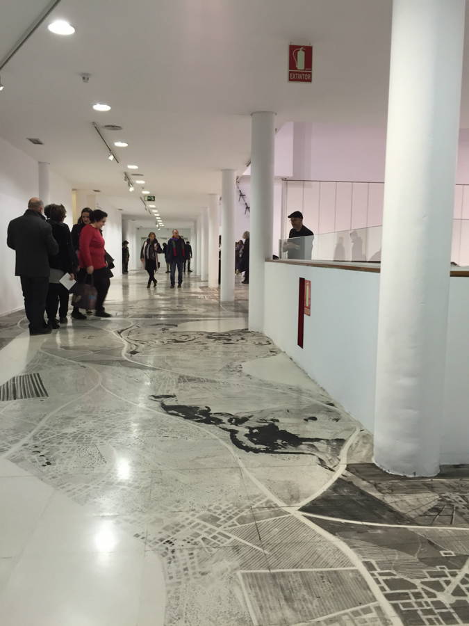 Visitors walking through a gallery with a reflective marble floor and red marking tape on the ground, from Daniel Muñoz's 'Trenches and Other Contraceptives'
