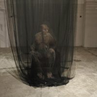 Dark room with a shrouded standing figure inside black netting