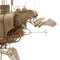 Sepia-toned photograph of a mechanical sculpture with pipes, a wheel, and a lever arm