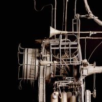 Photograph of a dark mechanical sculpture with horn and pipe forms against a black background