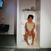 Photograph of a woman posing beside her own portrait painting in a doorway