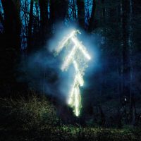 A glowing light-painted stick-figure robot shape in a dark forest, from 'The Robot Series' by Thomas Jackson