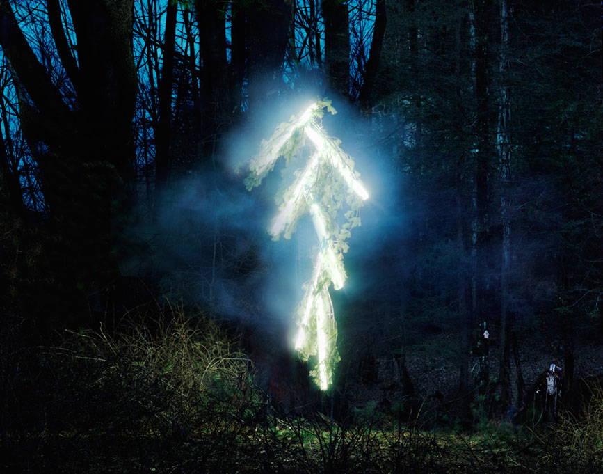 A glowing light-painted stick-figure robot shape in a dark forest, from 'The Robot Series' by Thomas Jackson
