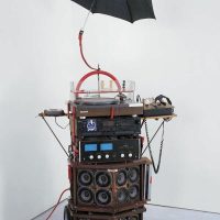 Sculptural wired boombox device with an open black umbrella suspended above it