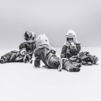 Black-and-white photograph of two seated sculptural astronaut figures in wrapped spacesuits