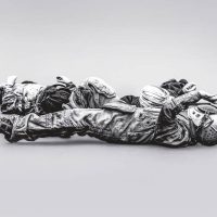 Black-and-white photograph of two reclining sculptural astronaut figures wrapped in bundled fabric