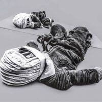 Black-and-white photograph of a reclining sculptural astronaut figure with a textured, paper-like surface