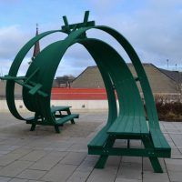 Large twisted green ribbon sculpture by Michael Beitz in a park setting, seen in daylight