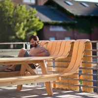 Wooden bench-and-table sculpture by Michael Beitz with a man seated at it outdoors near a brick building