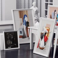 Styled room with framed abstract artworks and white sculptural busts arranged around a wooden table and easels