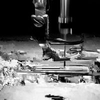 Abstract monochrome image of scattered debris around drill-like machinery, from Parisa Pakzamir's 'Tools of Destruction'