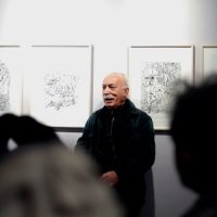 AbdolHossein Pazoki standing beside his framed line drawings at the Zero-One exhibition
