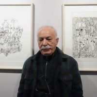 Artist Abdolhossein Pazoki standing in front of his framed drawings at Aliha Gallery