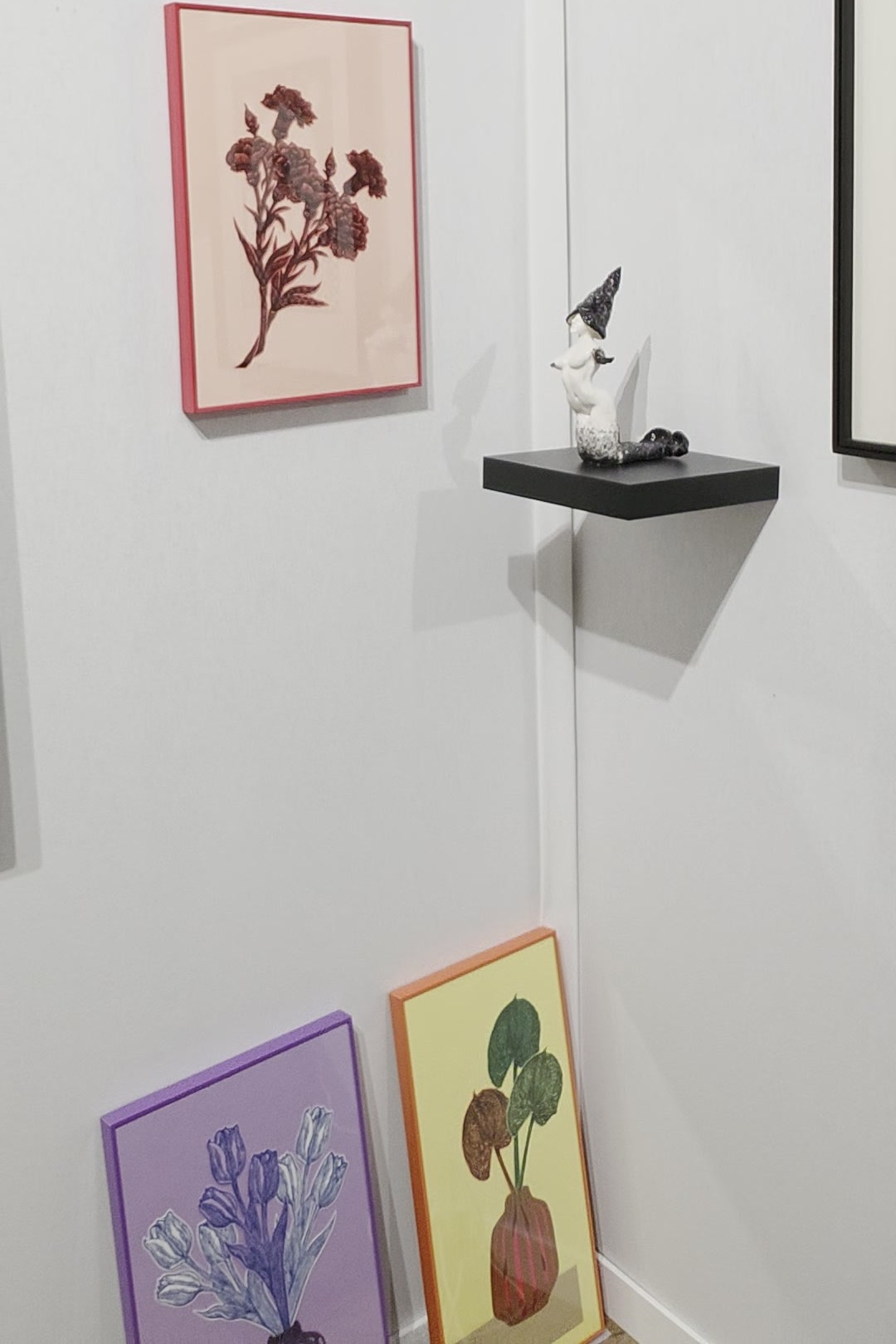 Angle du stand de la Galerie Keshavarzian : une œuvre aux œillets dans un cadre rouge, une petite figure sur une étagère noire et deux œuvres colorées encadrées posées contre le mur