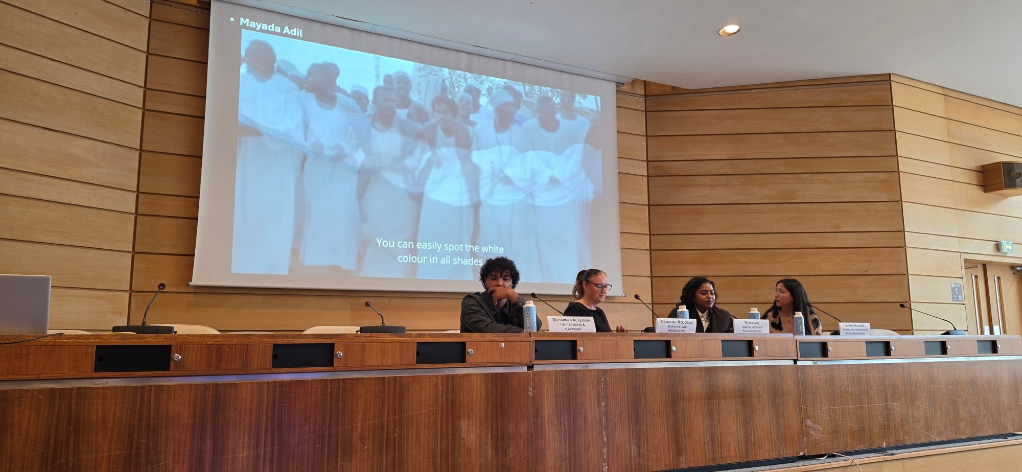 Image d’un film projeté montrant des personnes vêtues de blanc, avec le sous-titre « You can easily spot the white colour in all shades », au-dessus de la table du panel