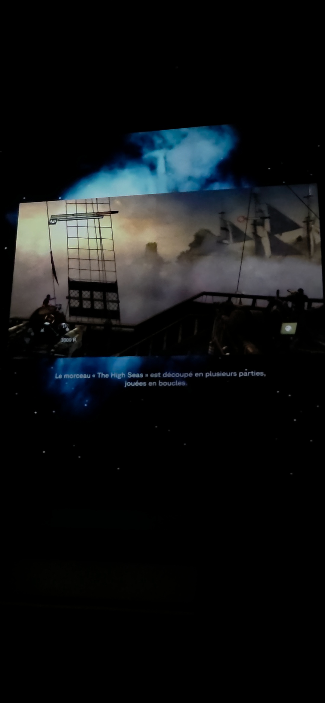 Une projection d’un voilier dans la brume, avec un cartel en français expliquant que le morceau The High Seas est découpé en plusieurs parties jouées en boucles