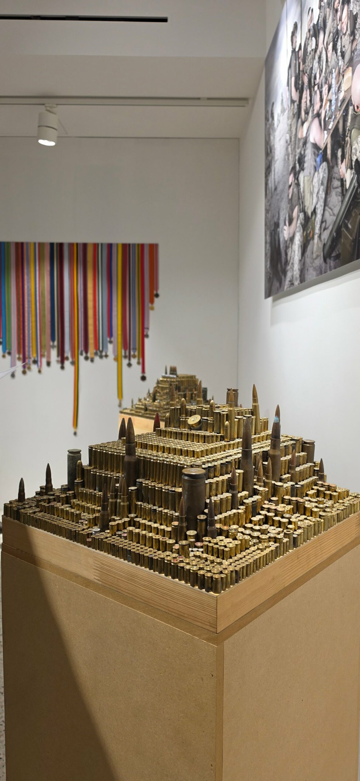 Structure en gradins, évoquant un temple, faite de cartouches dressées sur un socle en bois, avec un mur de rubans de médailles colorés suspendus derrière.